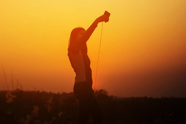 Silhouette woman taking photo of sunset by using smart phone