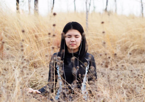 Азиатка медитирует на травяном поле — стоковое фото