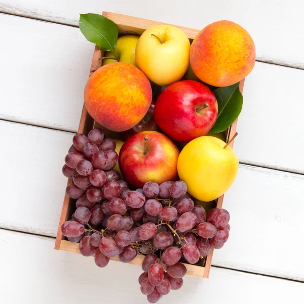 Pudełko owoców z jabłkami, brzoskwiniami i winogronami. Widok z góry. — Zdjęcie stockowe