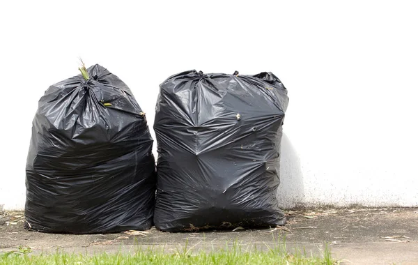 Schwarze Müllsäcke auf dem Gehweg und weißer Wandhintergrund — Stockfoto