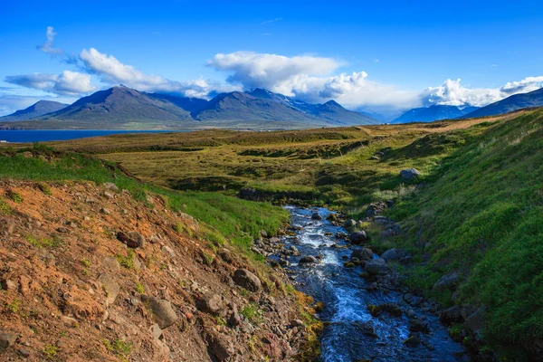 Underbara isländska landskapet. gräs-mark, sjö, höga mångfärgade berg och vacker himmel. — Stockfoto