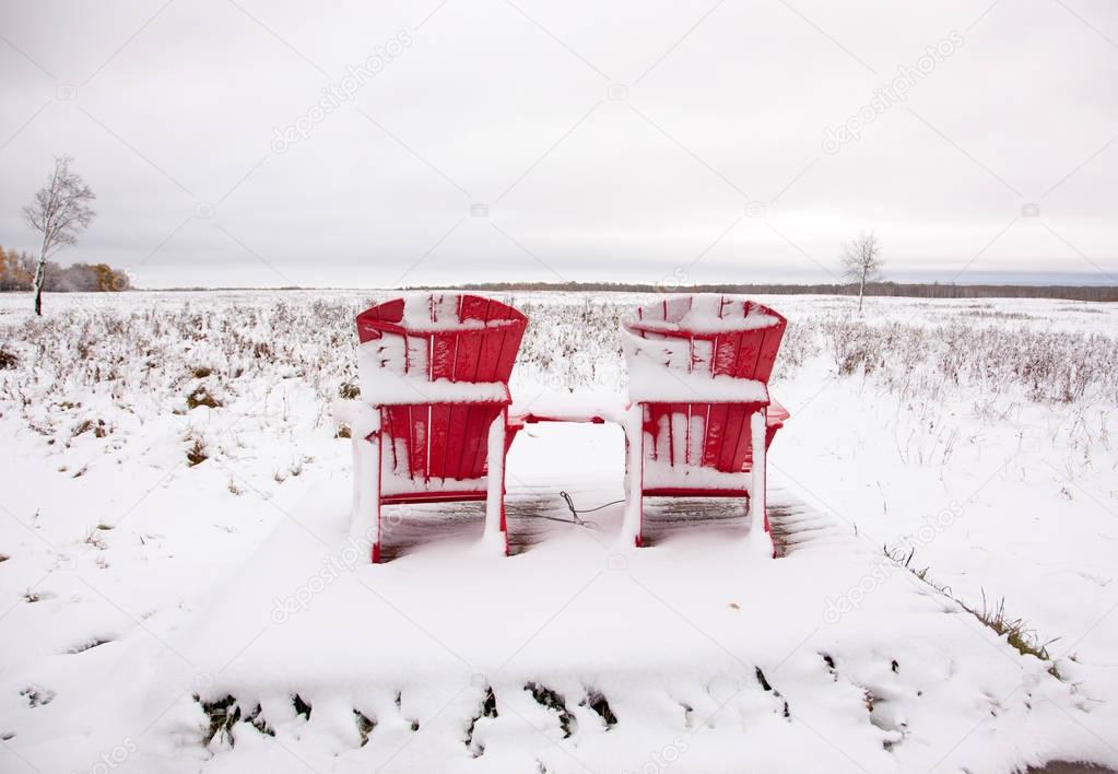 two red Adirondack chairs on snowy field 