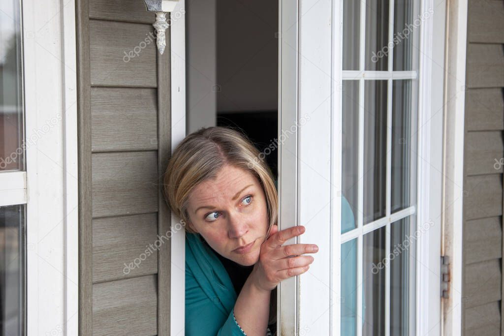 a woman peeks out her front door wondering if it is safe to leave