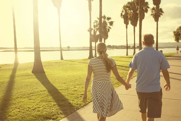 Atrás da vista de um casal de meia idade andando juntos de mãos dadas — Fotografia de Stock