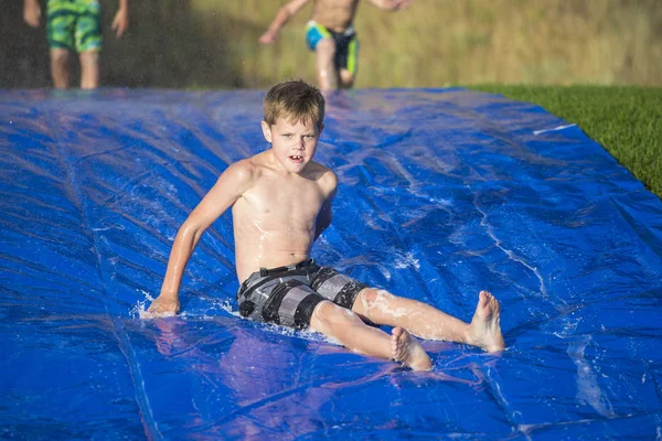 Young boy sliding down a slip and slide outdoors — Stock Photo, Image