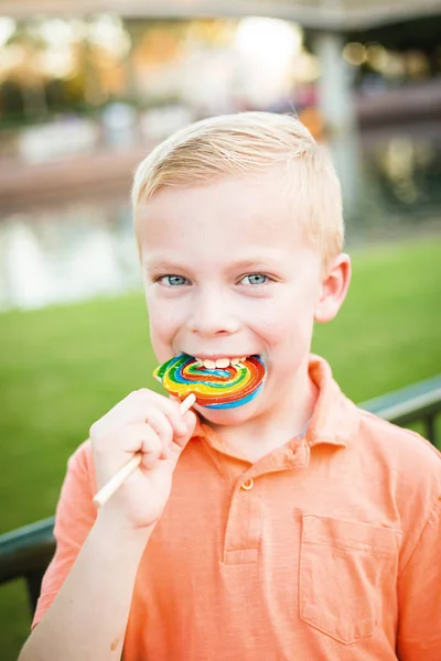 Schattige jonge jongen likken een grote kleurrijke lolly in de buitenlucht — Stockfoto