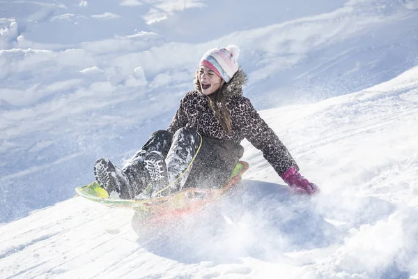 Blij en opgewonden meisje rodelen afdaling op een besneeuwde dag. — Stockfoto