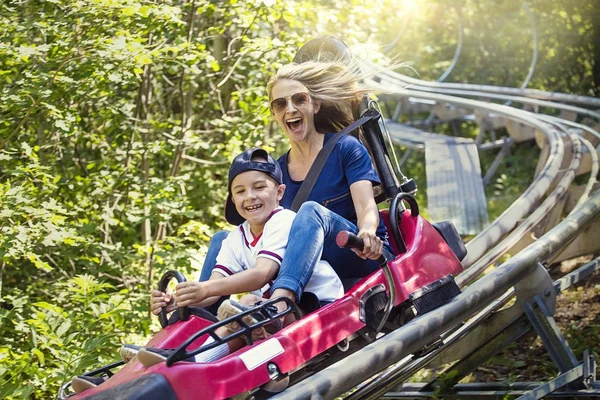 笑顔の女性と彼女の暖かい夏の日に屋外のローラー コースターに一緒に乗って下り坂の男の子 彼女は楽しい式彼らは遊園地赤に乗ってスリリングな乗り心地を楽しむ — ストック写真