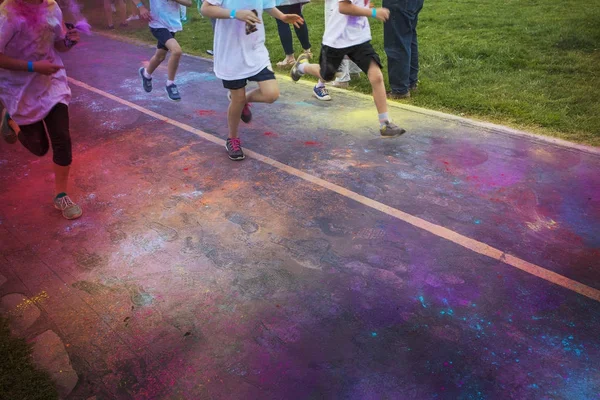 Abstract photo of a group of runners running in a color run race event. No faces visible on the legs and the feet and shoes of the runner. Lots of colorful clouds of chalk in the air and on the street