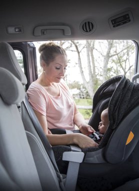 Anne araba sürmeden önce tatlı çocuğunu emniyet kemerine bağlayıp kemerini takıyor. Ebeveyn, bebek için arka koltuğun güvenliğini kontrol ediyor.