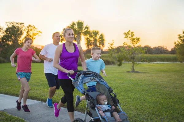 健康的年轻家庭在户外散步和慢跑 沿着公园里铺好的人行道 在日落时分推着婴儿车 — 图库照片