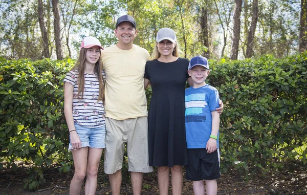 Cute young family portrait all wearing baseball hats outdoors. Smiling and showing off their different caps they have on their heads