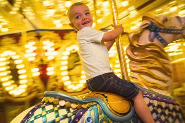 Küçük şirin bir çocuk lunaparkta ya da karnavalda atlıkarıncaya binerken eğleniyor. Mutlu küçük çocuk atlıkarıncaya biniyor parlak ışıklarla dolanıyor