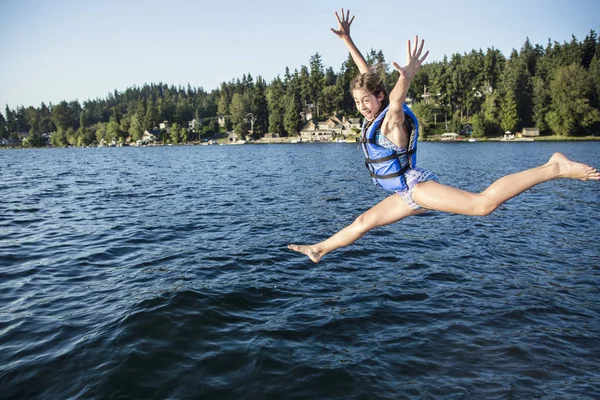 一个快乐的女孩从码头跳到一个美丽的高山湖中 有一个暑假的乐趣 她脸上激动的表情和胳膊高高地抬起来 — 图库照片
