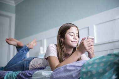 Ergenlik öncesi ergenlik çağında bir kız evde yatakta akıllı bir telefonla mesajlaşıyor. Ön plana odaklan ve boşluğu kopyala