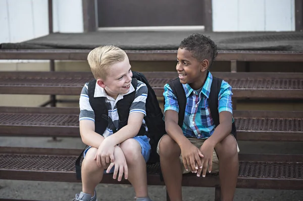 两个学生在学校一起聊天的照片 笑着一起玩的男孩坐在楼梯上享受他们的友谊 — 图库照片
