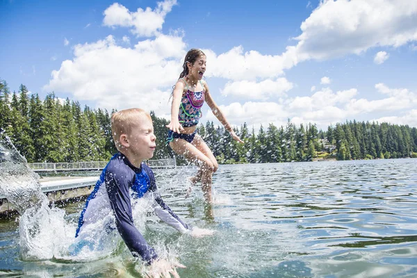 一个小男孩和一个小女孩从船坞跳到一个美丽的高山湖中 有一个暑假的乐趣 泼洒和弄湿 — 图库照片