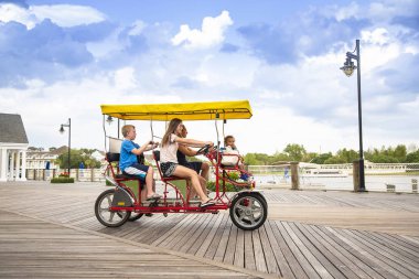 Geniş bir okyanus kıyısında çifte surrey bisiklet süren mutlu genç bir aile. Çocuklarla açık hava eğlencesi.