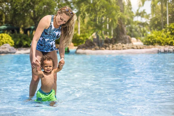 プールで息子と遊んでいる美しい若い母親 熱帯のリゾートで休暇中に水で遊んでいる混合レースの小さな男の子を笑っています コピースペース付きの全長写真 — ストック写真