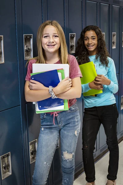 Portrait of two diverse female Junior High school Student standing in a school hallway. Smiling school girls looking and holding their books during breaks in the day