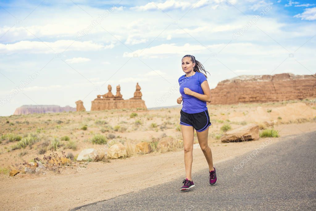 Beautiful fit woman in her 30s running on a paved trail in a scenic desert park. The healthy woman stays fit even on vacation with rocky sandstone cliffs in the background