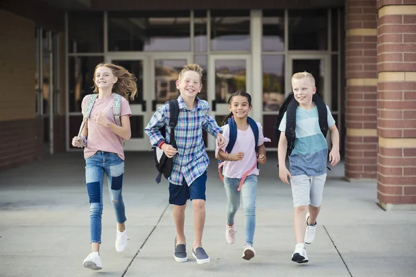 1日の終わりに小学校を出るときに走っている子どもたちのグループ 学校から幸せと興奮して家に帰る 学校の写真に戻る — ストック写真