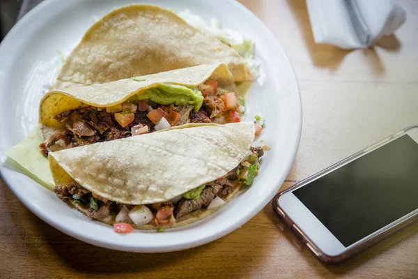 墨西哥一家餐馆里 三个美味的玉米卷放在盘子里 旁边坐着一部手机 网上订购食物和午餐的概念 — 图库照片