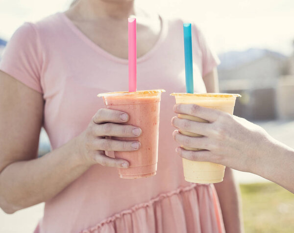 Closeup of two people holding healthy fruit smoothie drinks in their hands. Outdoor photos with focus on the smoothies. Eating healthy and treating your body well