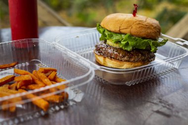 Açık hava restoranına gitmek için açık plastikte marullu ızgara sığır etli hamburger ve ananas. Tatlı patates kızartmasıyla servis edilir.
