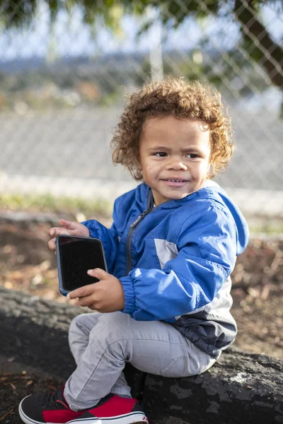 一个多样化的小男孩在户外公园用他父母的智能手机 正在被抚养的依赖屏幕的儿童的概念照 — 图库照片