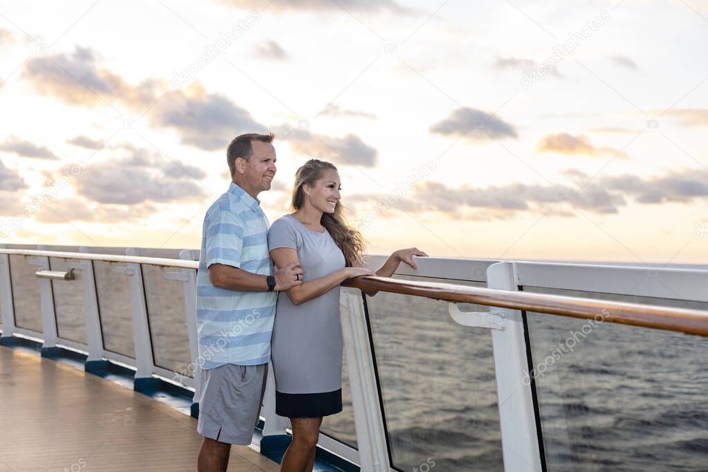 Middle aged couple enjoying a Caribbean Cruise vacation together. Candid photo of a couple enjoying their time on board a cruise ship together. Walking along the deck at sunset and laughing together