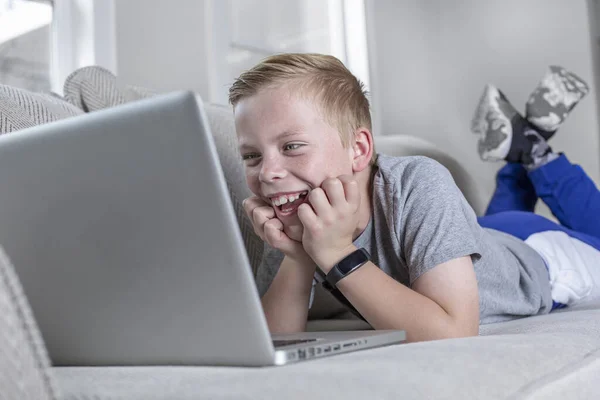 Menino Sorridente Feliz Estudando Casa Usando Laptop Deitado Sofá — Fotografia de Stock