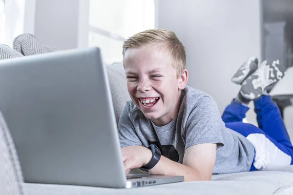 Szczęśliwy Uśmiechnięty Chłopiec Uczy Się Domu Pomocą Laptopa Leżąc Kanapie — Zdjęcie stockowe