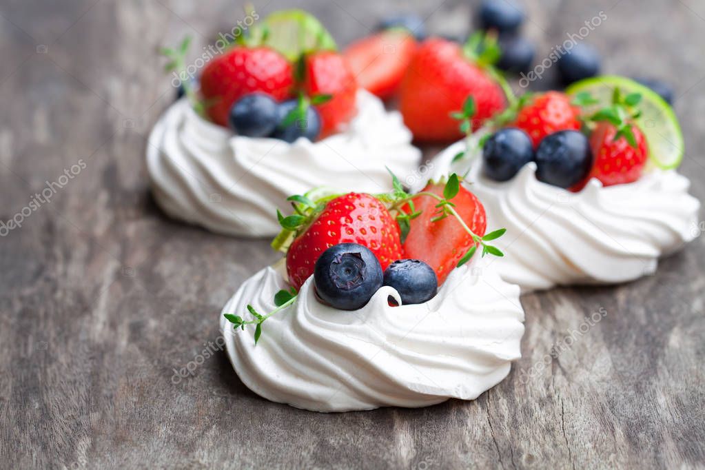 Mini  Pavlova meringue cakes with berries and lime on rustic woo