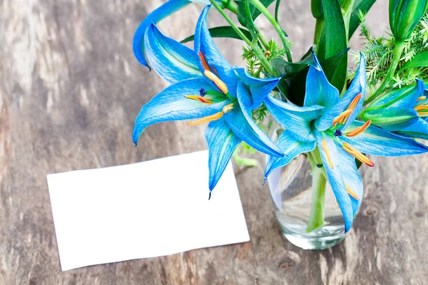 blue  lilies on the rustic wooden table with sheet of paper
