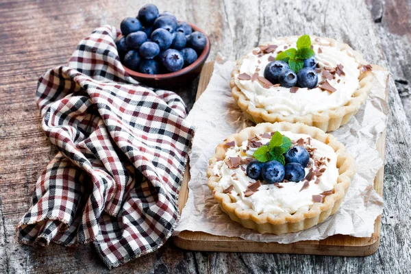 Heerlijke taarten met slagroom en verse bosbessen op houten tafel — Stockfoto