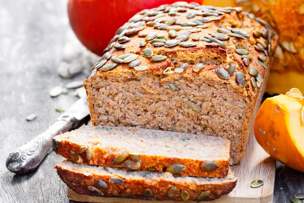 Sliced  pumpkin bread loaf on wooden cutting board with seeds