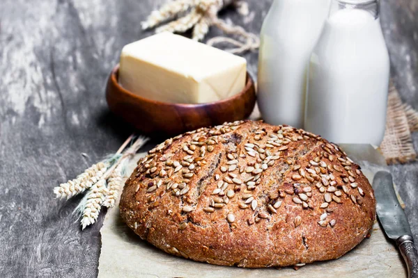 Homemade  rye bread on baking paper and bottles of milk on woode — Stock Photo, Image