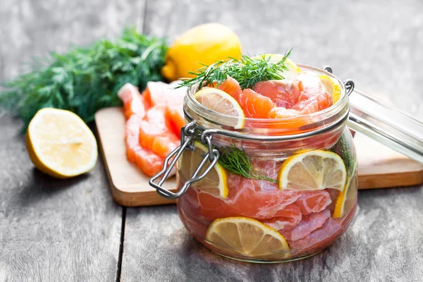 Salted  salmon with lemon in glass jar on wooden background