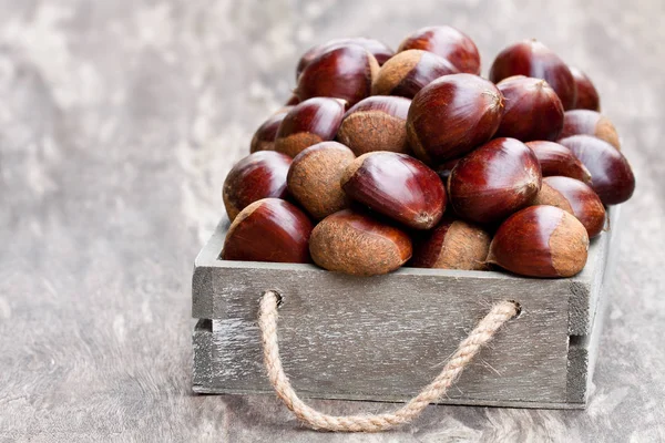 Fresh  raw chestnuts in a wooden box on wooden background — Stock Photo, Image