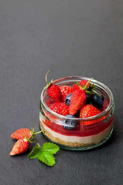Mini  wild forest berries cheesecake in a glass pot on black sto