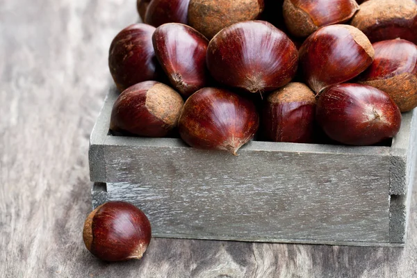 Fresh  raw chestnuts in a wooden box on wooden background — Stock Photo, Image