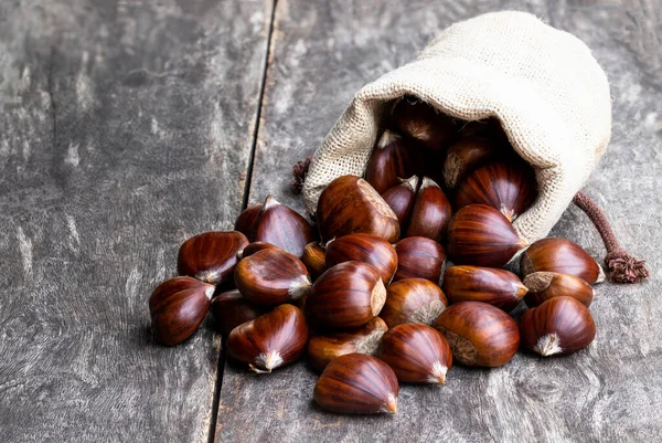 Fresh chestnut scattered of the burlap bag on wooden table — Stock Photo, Image