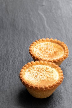 Lezzetli taze pişmiş yumurtalı tartlar, siyah taş arka planda. 