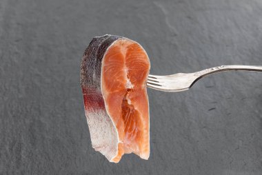 Siyah taş arka planda çatalla gökkuşağı alabalığının tuzlu dilimi 