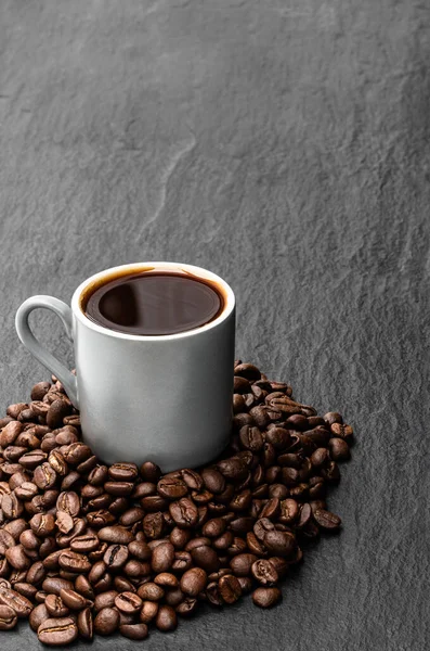 黒石の背景に豆と小さなカップで黒コーヒー — ストック写真