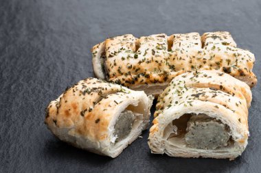 Siyah taş arka planda otlarla kaplı puf böreğin içindeki sosis eti. 