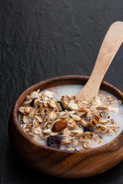 Sağlıklı kahvaltı müsli ve granola. Siyah taş arka planda, berrak bardakta yağsız süt. 