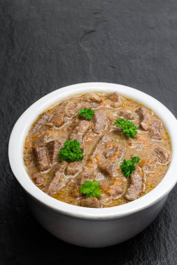 Siyah taş arka planda kil kasede sebzeli sığır güveci. 