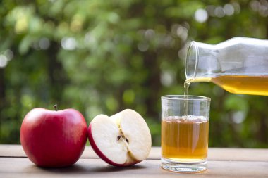 Elma suyu ahşap zemine ve Bokeh arka planına kırmızı elmalardan dökülüyor